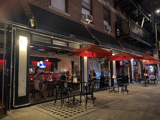 Hell’s Kitchen NYC restaurants at night with warm dining room lights, 9th Avenue energy, and Broadway visitors walking west of Times Square