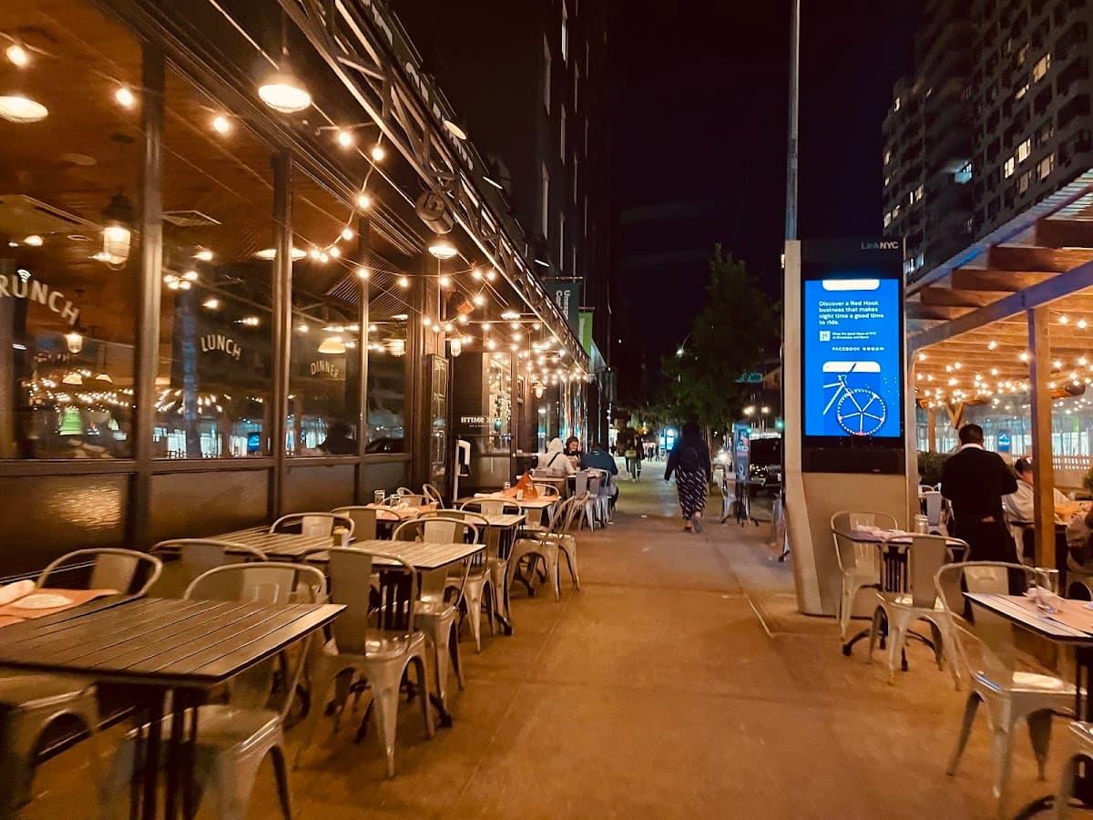 Hell’s Kitchen NYC restaurants at night with warm dining room lights, 9th Avenue energy, and Broadway visitors walking west of Times Square