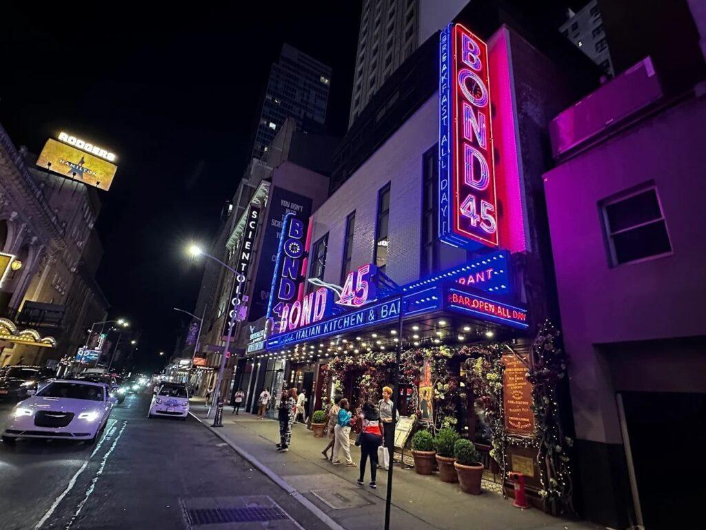 Theater District NYC restaurants near Broadway with Restaurant Row dining, theater marquees, and pre-show crowds at night