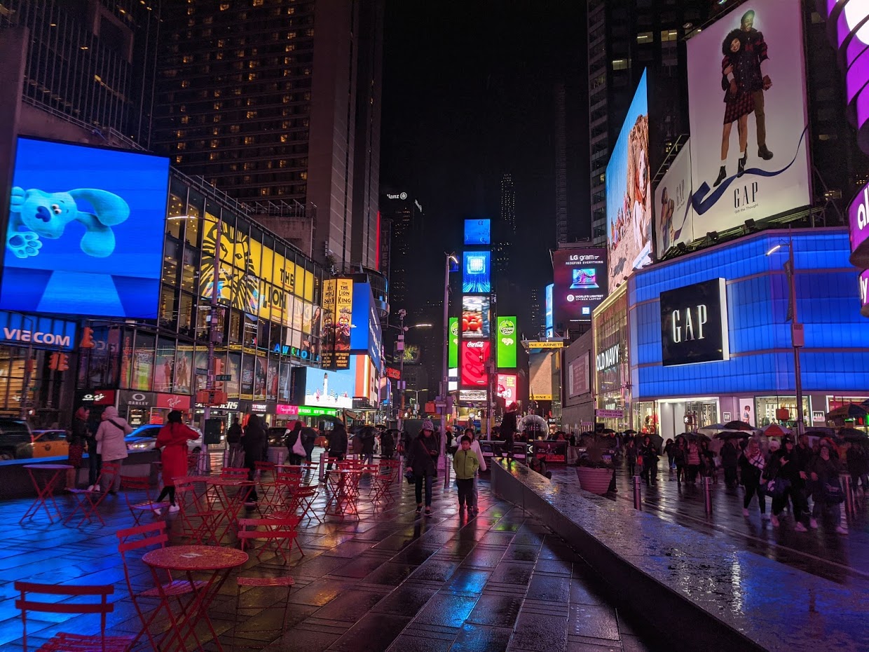 Times Square on a rainy night in New York City, near Broadway theaters and show-night crowds.