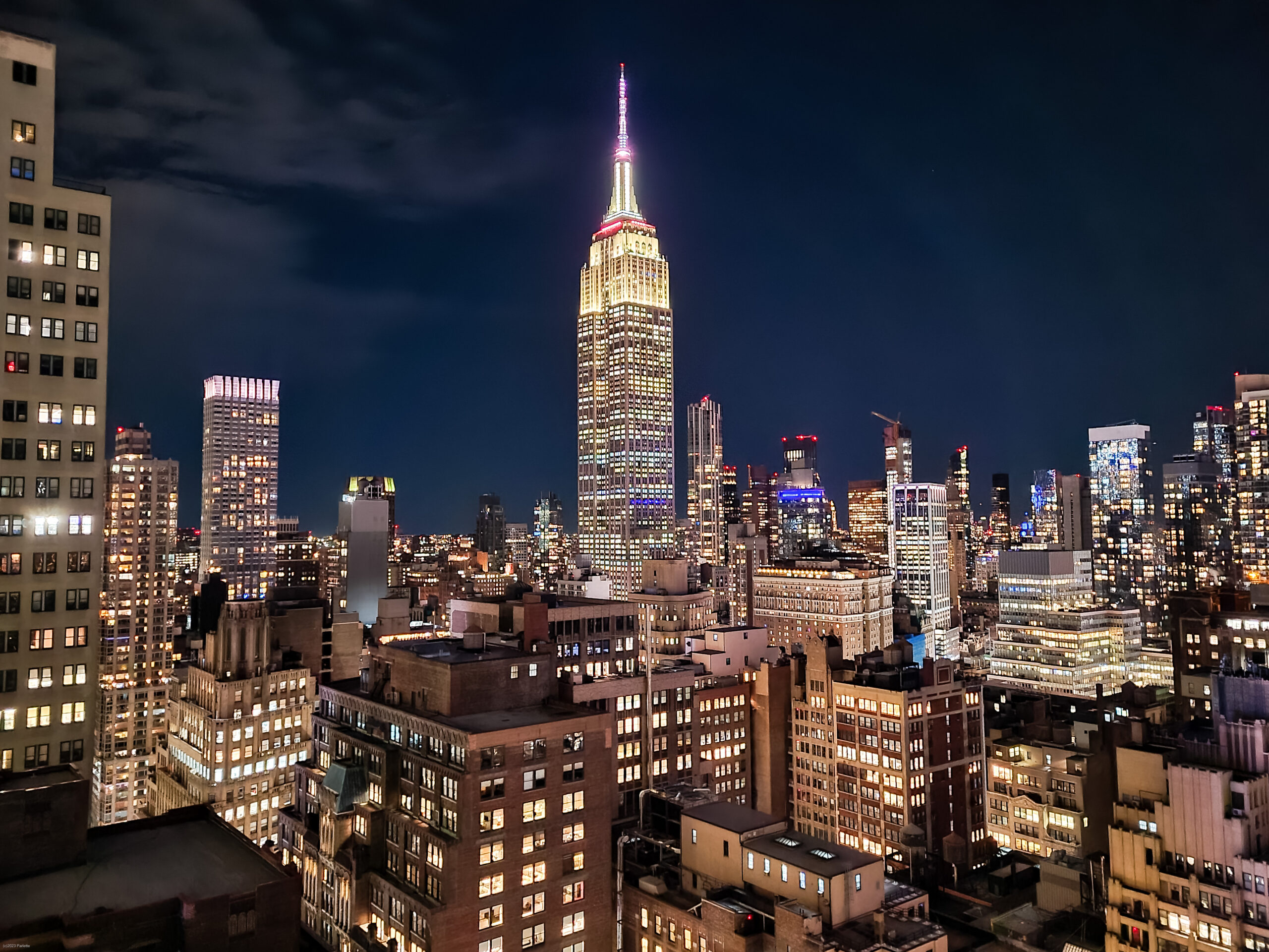 Empire State Building and Midtown Manhattan skyline at night from a rooftop bar near Times Square, a romantic NYC rooftop date-night view.