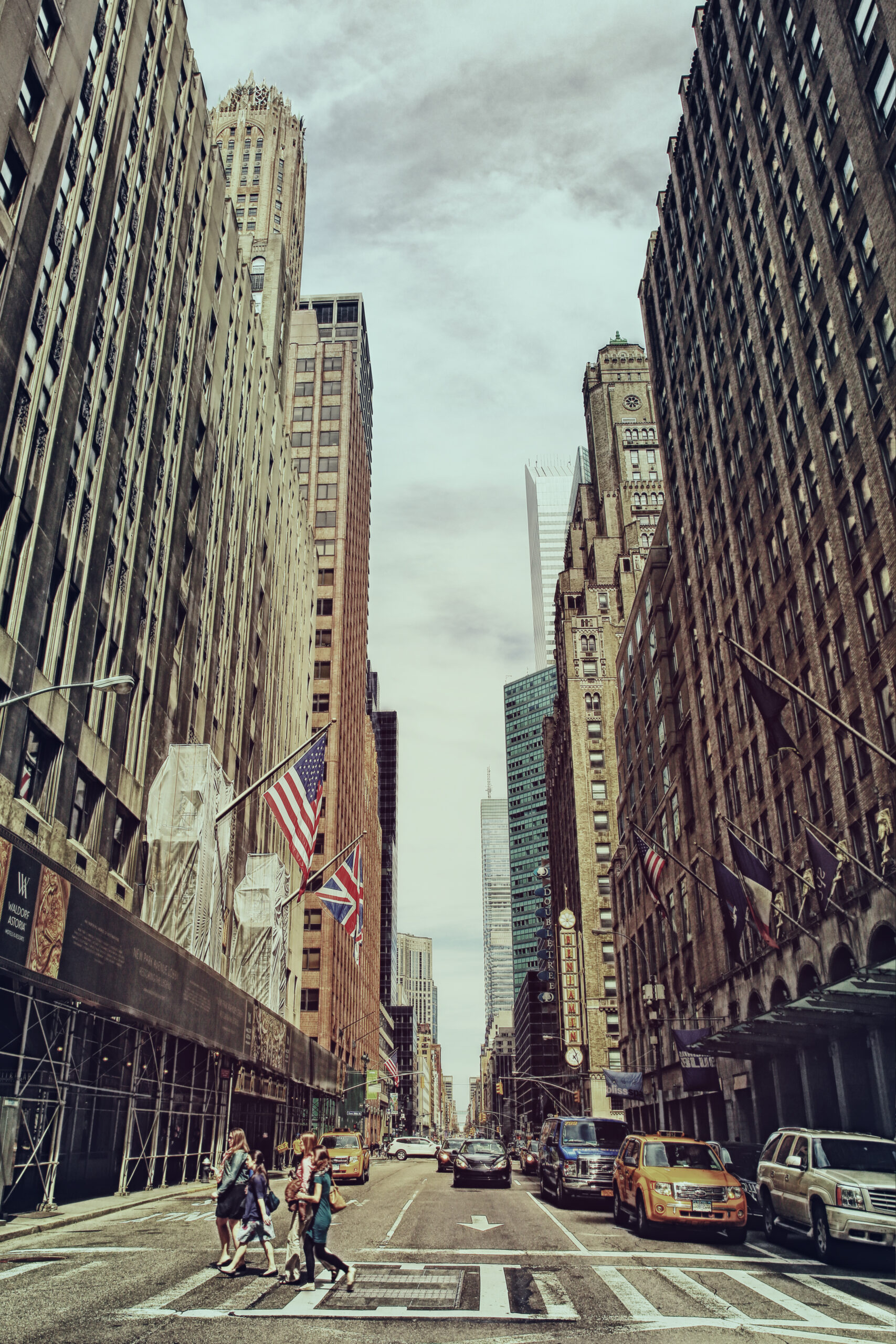 People walking across a busy New York City street with tall buildings and traffic in the background